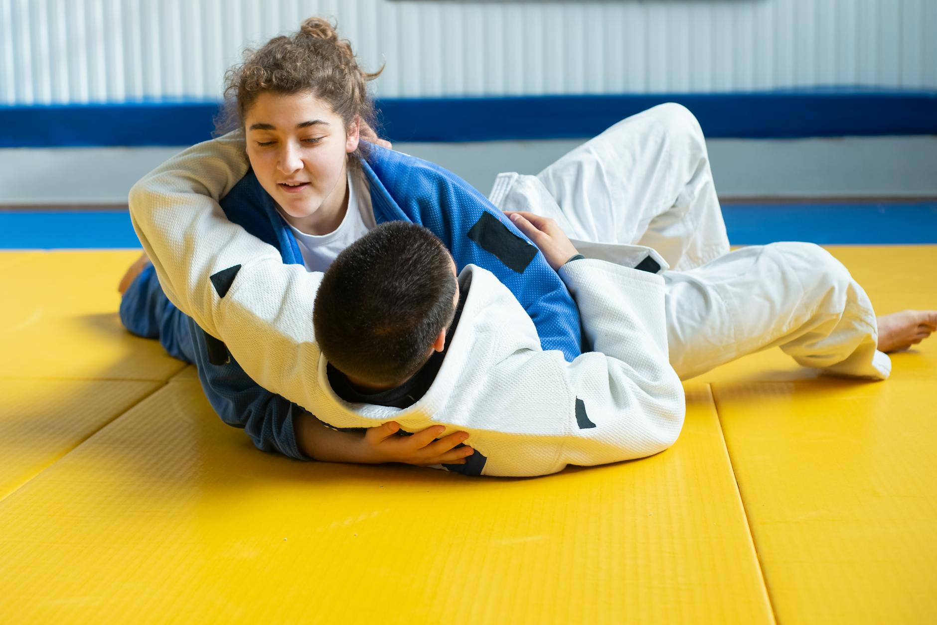Dwóch judoków trenuje techniki judo na żółtej macie w sali treningowej