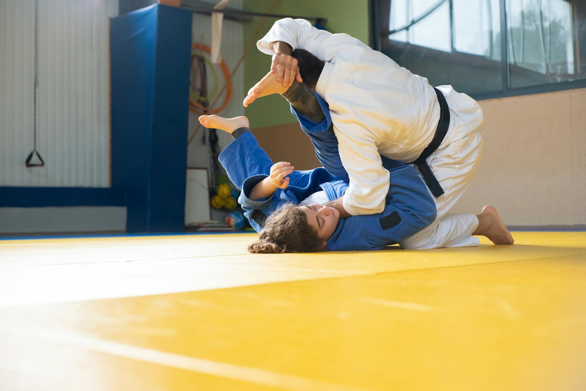 Dwoje dorosłych trenuje judo na żółtej macie w sali treningowej