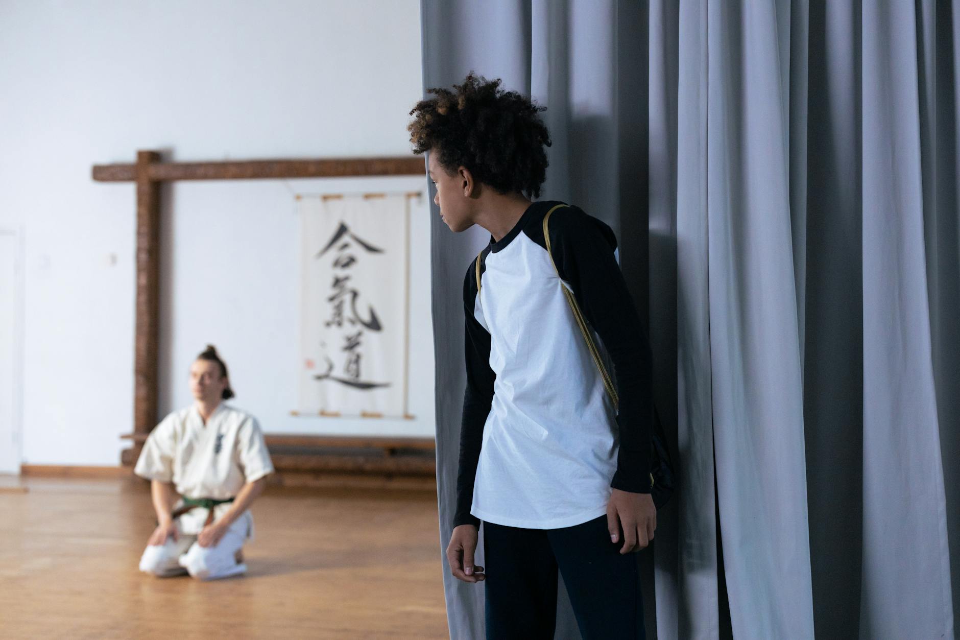 Chłopiec obserwuje trening judo w dojo, obok klęczy ćwiczący zawodnik