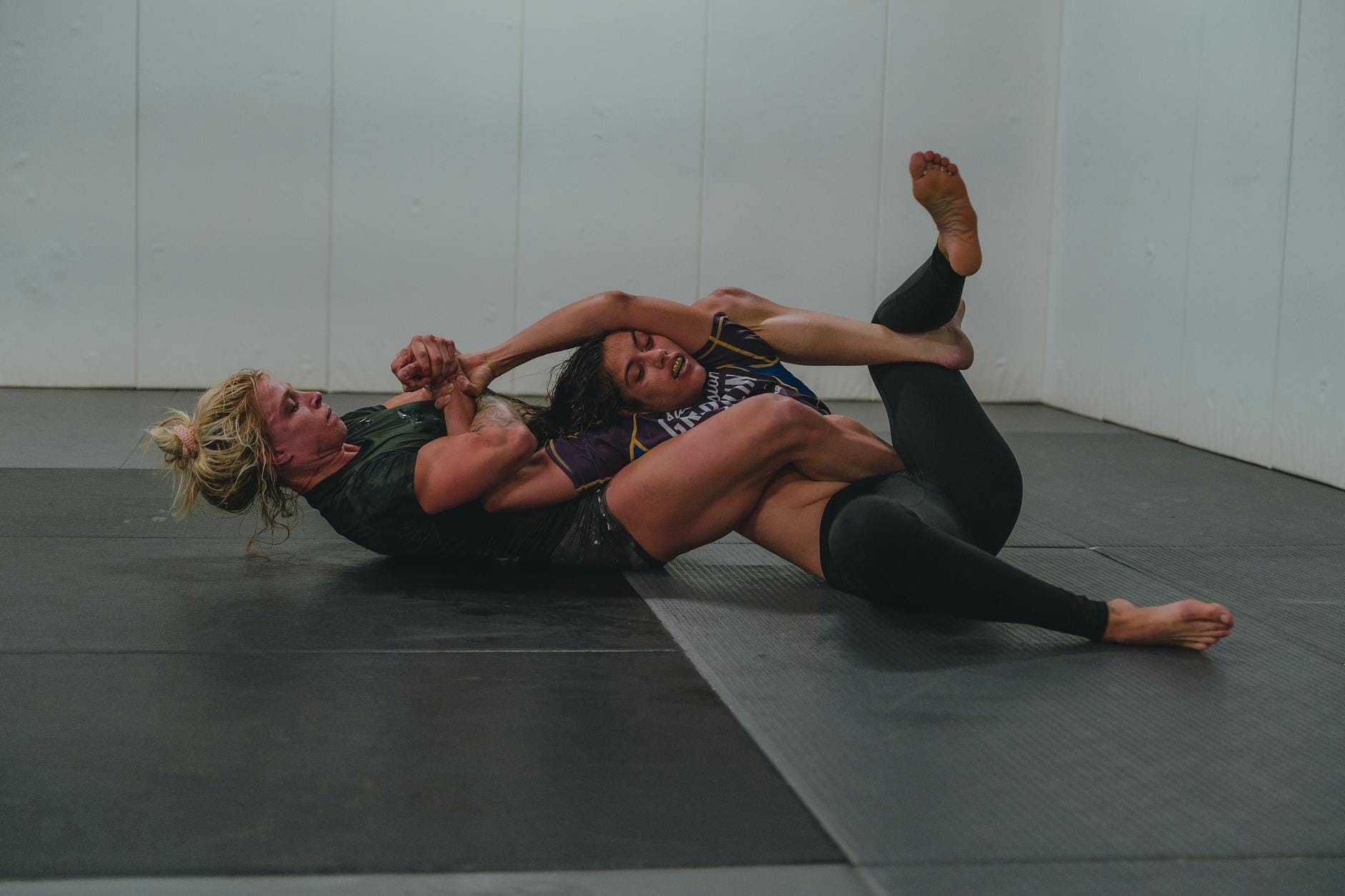 Dwie kobiety trenują grappling na macie w sali sportowej