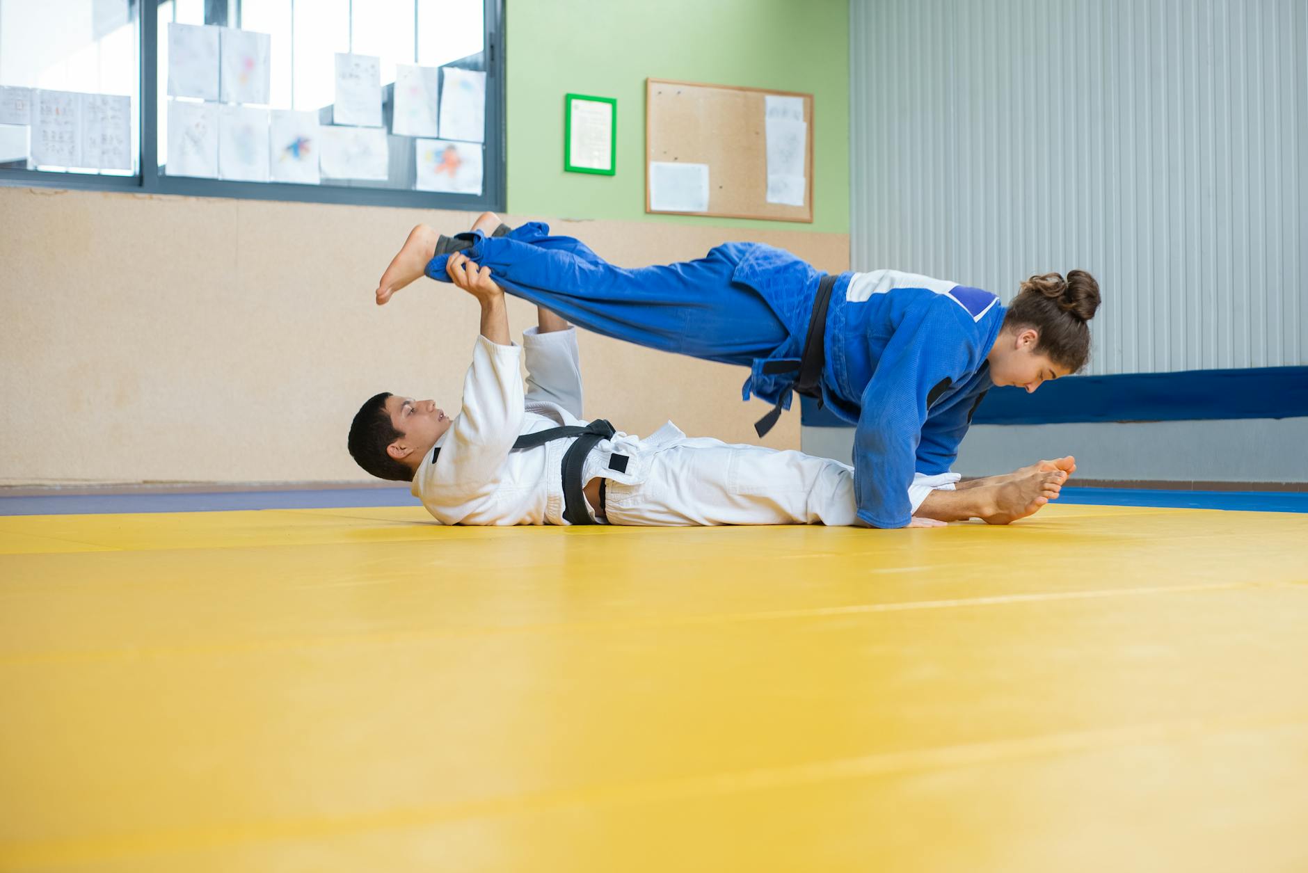 Dwóch judoków ćwiczy techniki ashi waza na żółtej macie w dojo