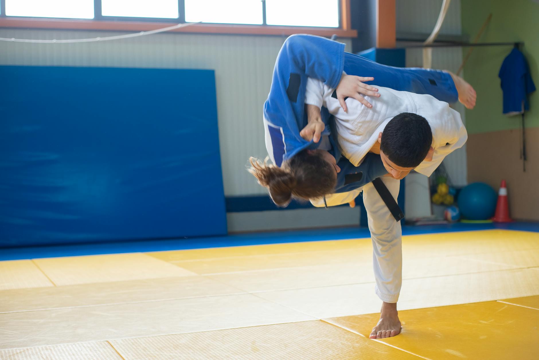 Dwóch judoków trenuje rzut na macie tatami w hali