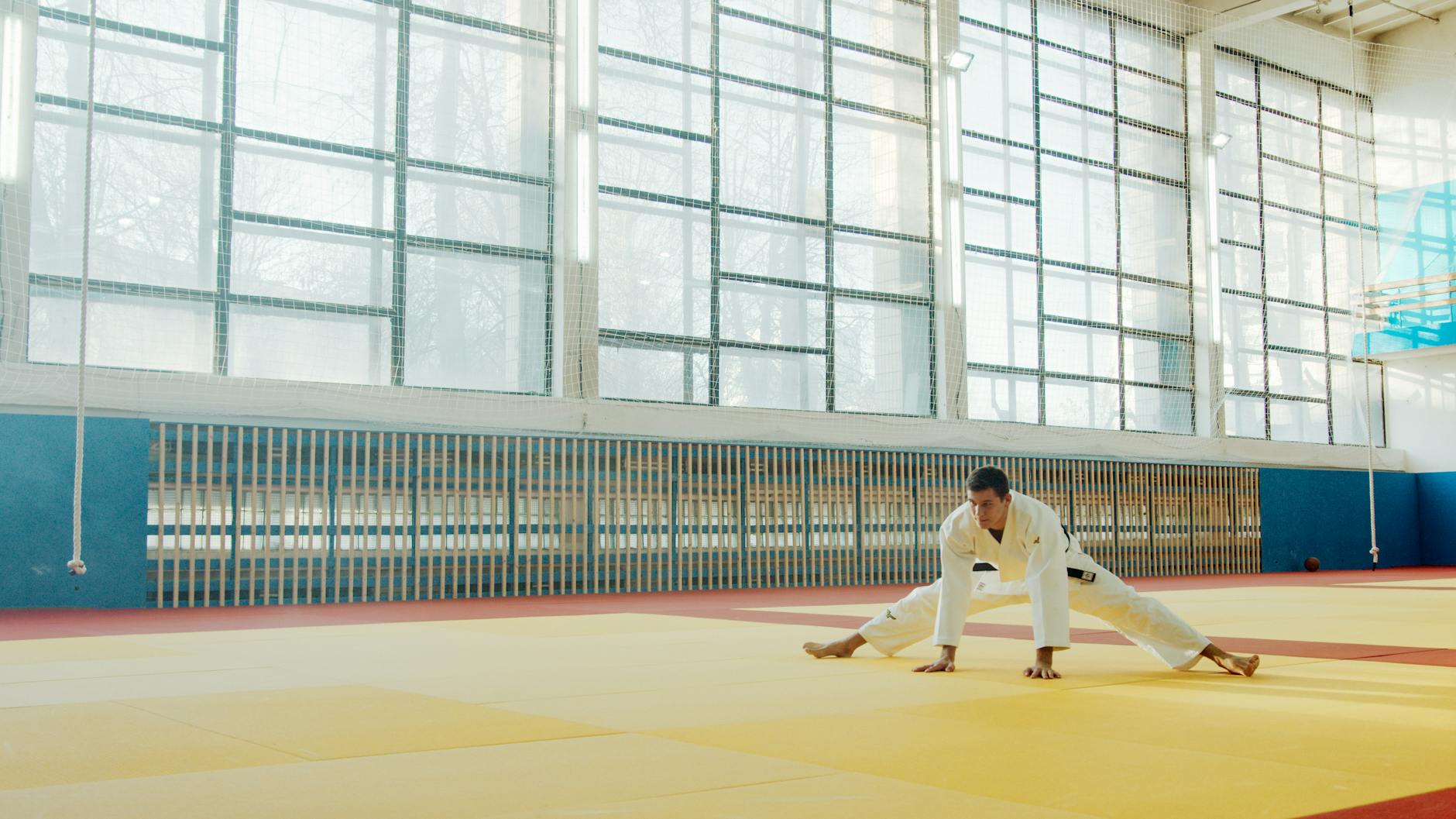 Judoka w kimonie rozciąga się na macie w jasnej sali treningowej