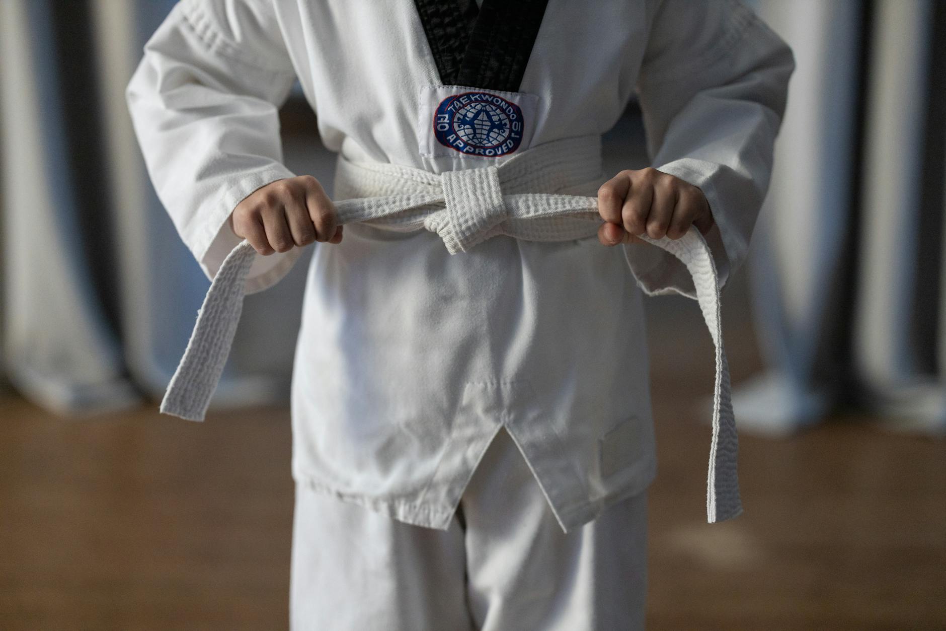 Początkujący karateka w kimonie wiąże biały pas przed treningiem
