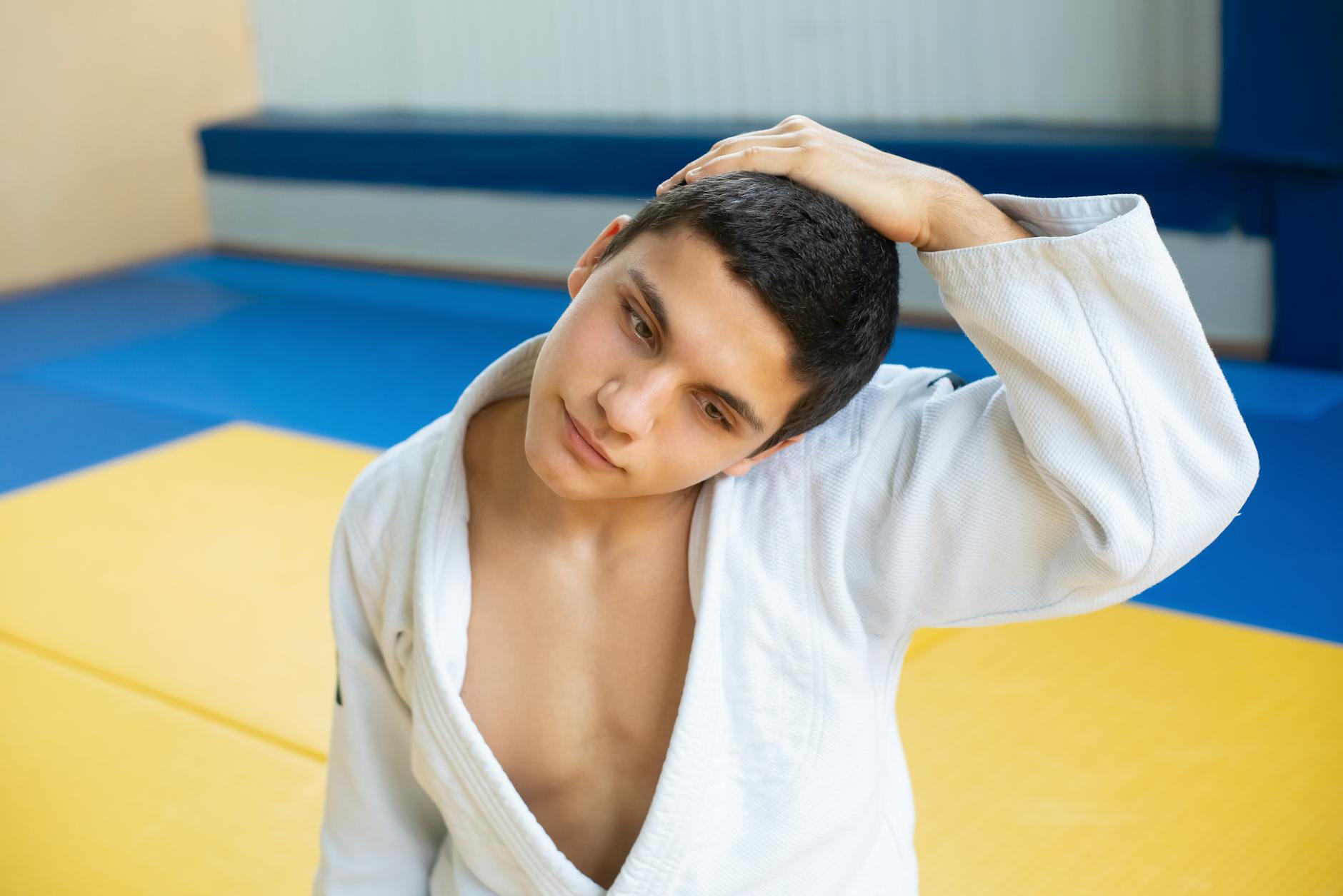 Zawodnik judo w dresie rozciąga kark na kolorowej sali treningowej