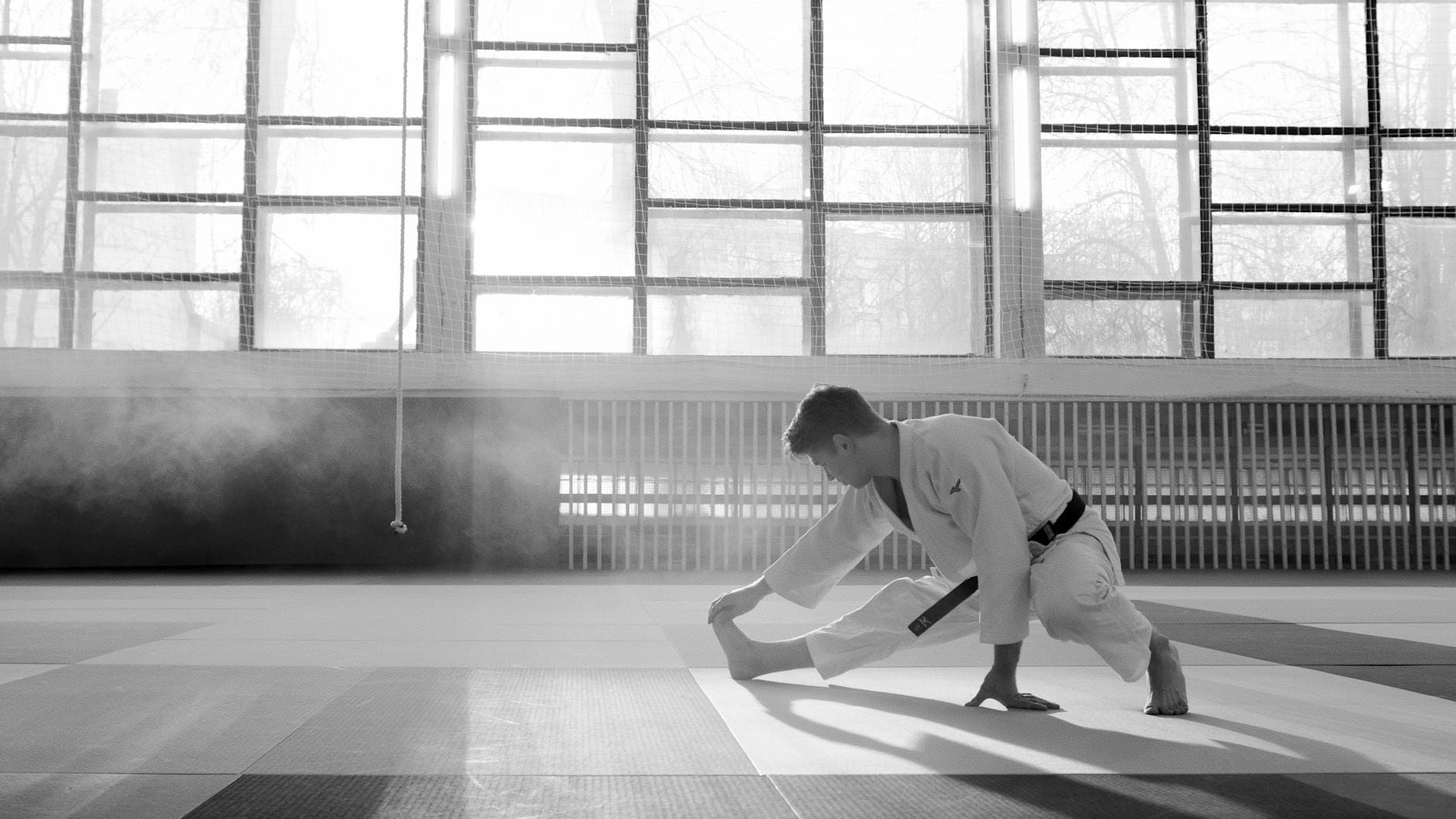 Zawodnik judo w kimonie rozciąga się w jasno oświetlonym dojo