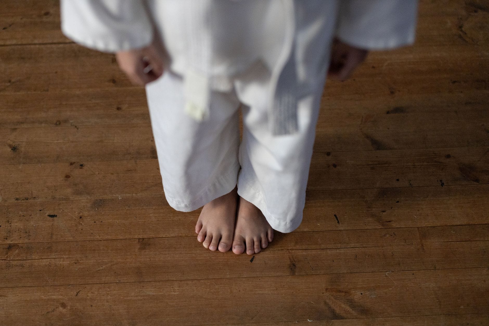 Jak rozpoznać dobry klub judo dla początkujących: pytania do trenera i rzeczy, na które warto zwrócić uwagę Dziecko w białym stroju judo boso stoi na drewnianej podłodze