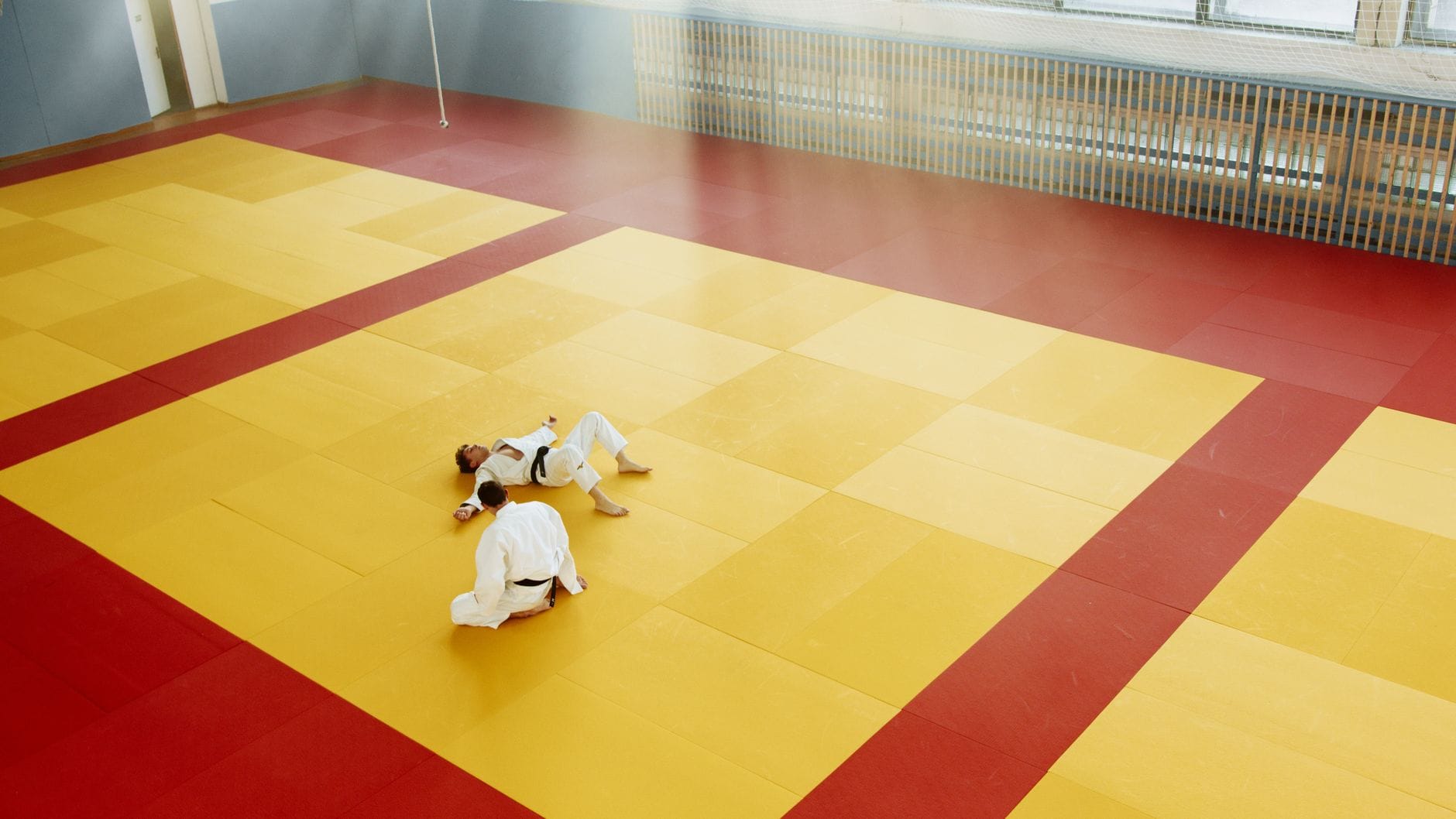 Dwóch judoków trenuje rzuty na kolorowej macie w dojo