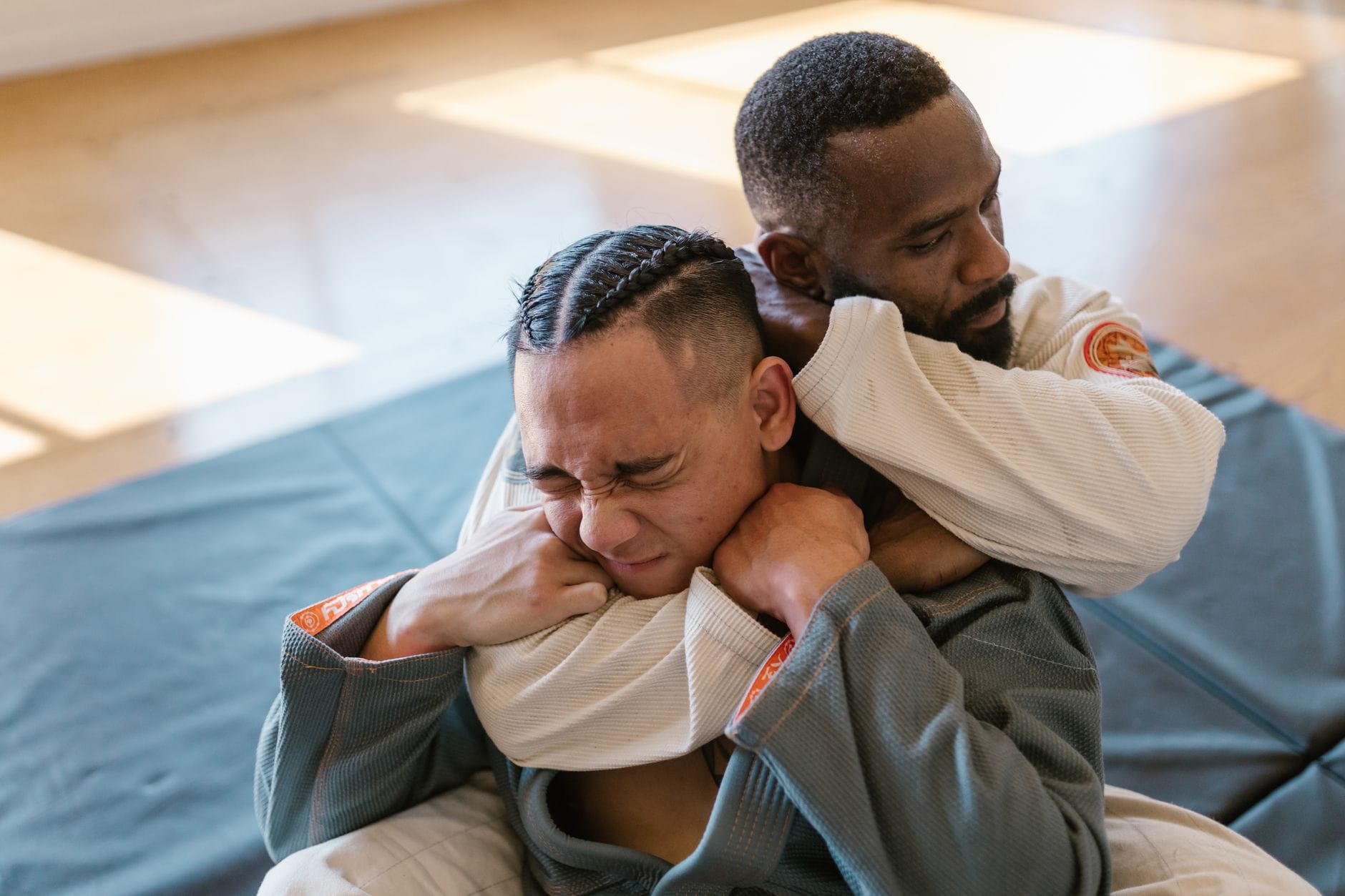 Dwóch zawodników BJJ trenuje sankaku w parterze na macie indoors