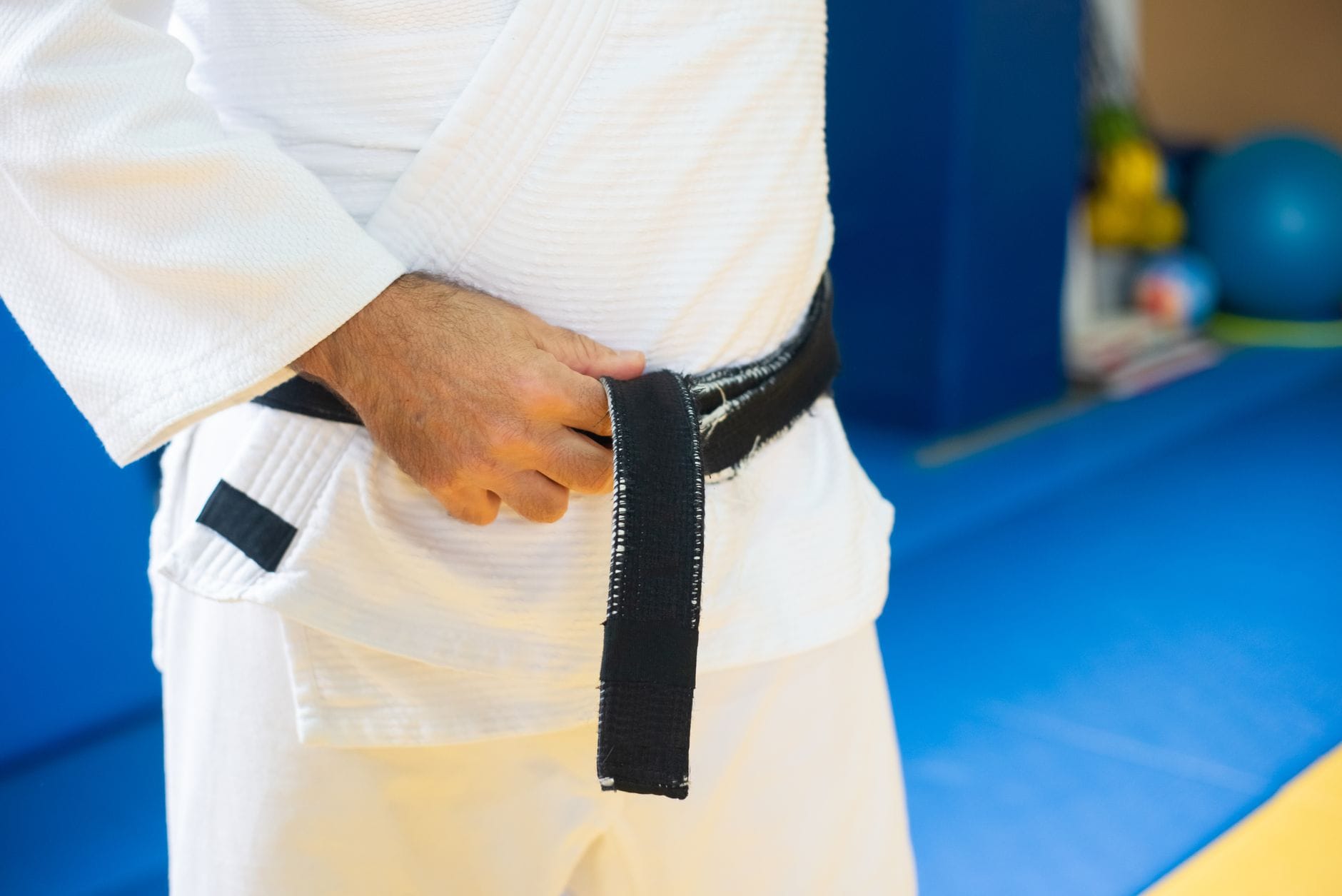 Przyrządy do wzmacniania chwytu dla judoki co ma sens a co to gadżety Judoka w białym kimonie zawiązuje czarny pas przed treningiem