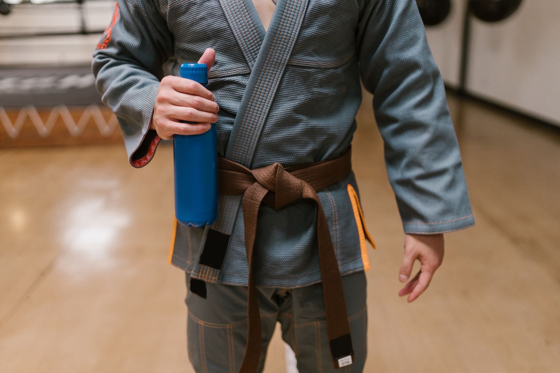 Judoka z brązowym pasem trzyma niebieską butelkę w sali treningowej