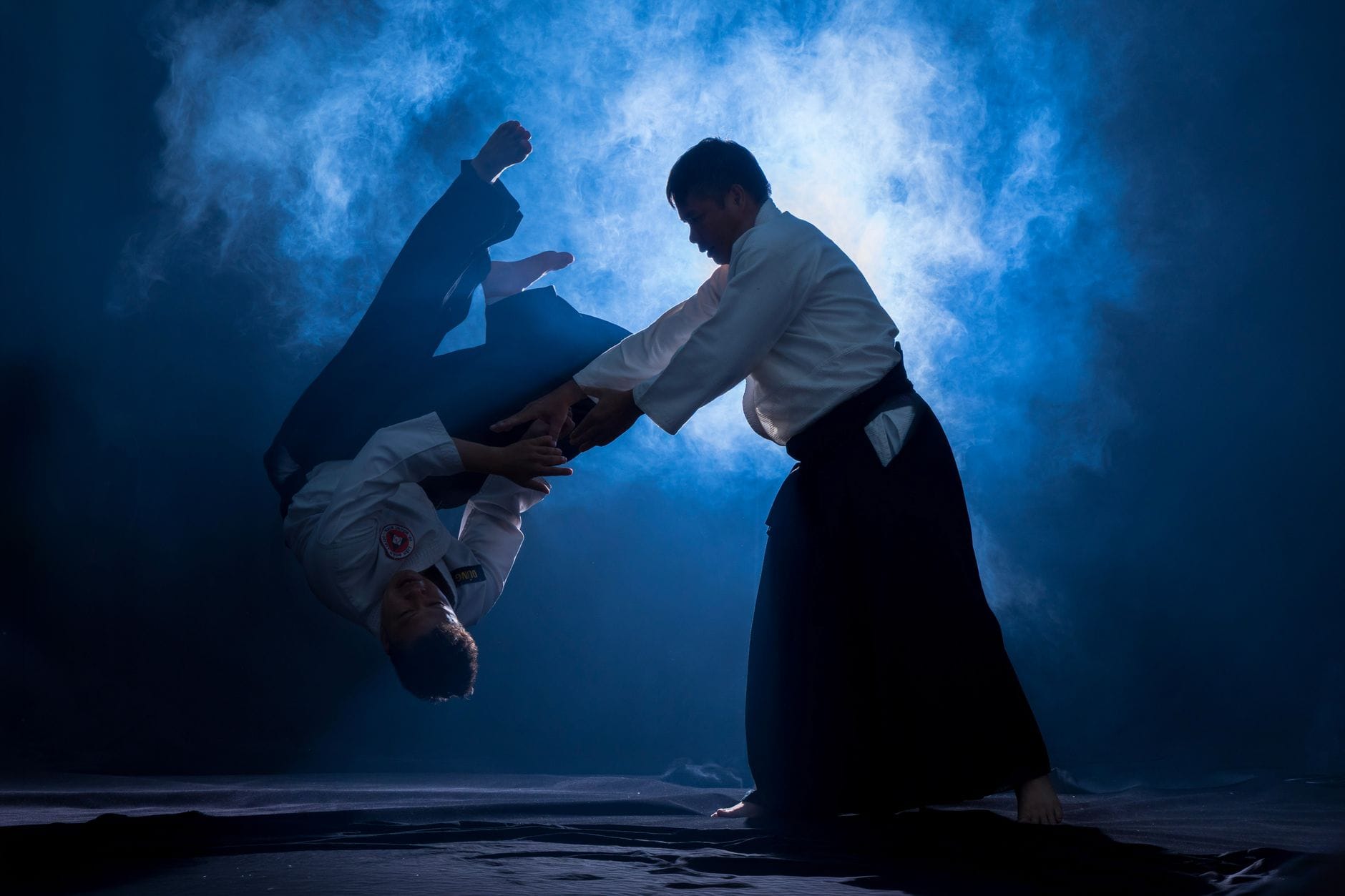 Dwóch adeptów aikido ćwiczy dynamiczny rzut w zadymionej sali
