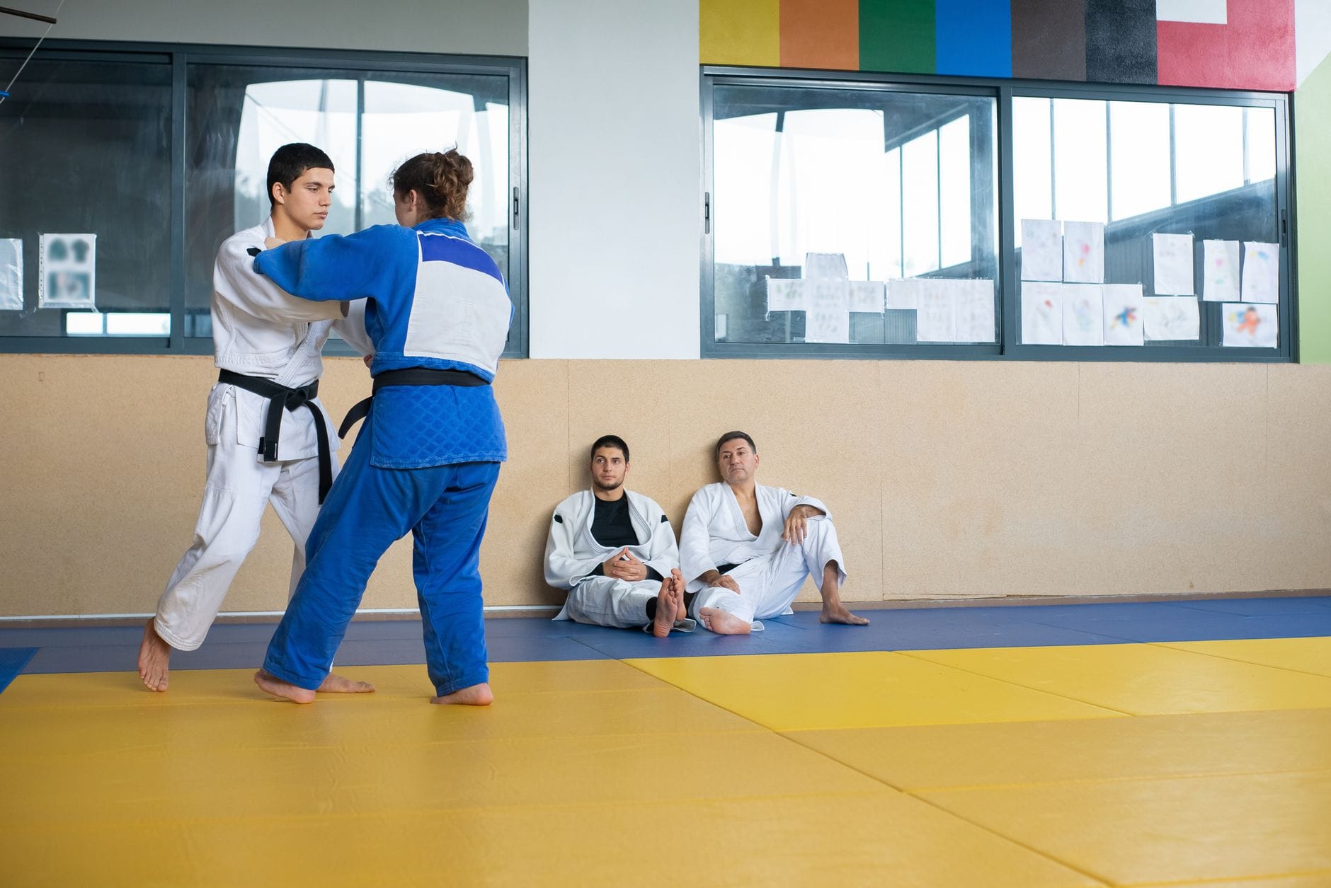 Judocy trenują rzuty na macie dojo, reszta grupy obserwuje ćwiczenie